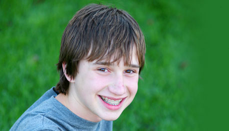 boy with braces smiling outside on grass