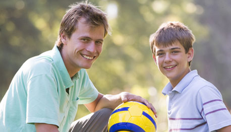 smiling father and son outside playing soccer